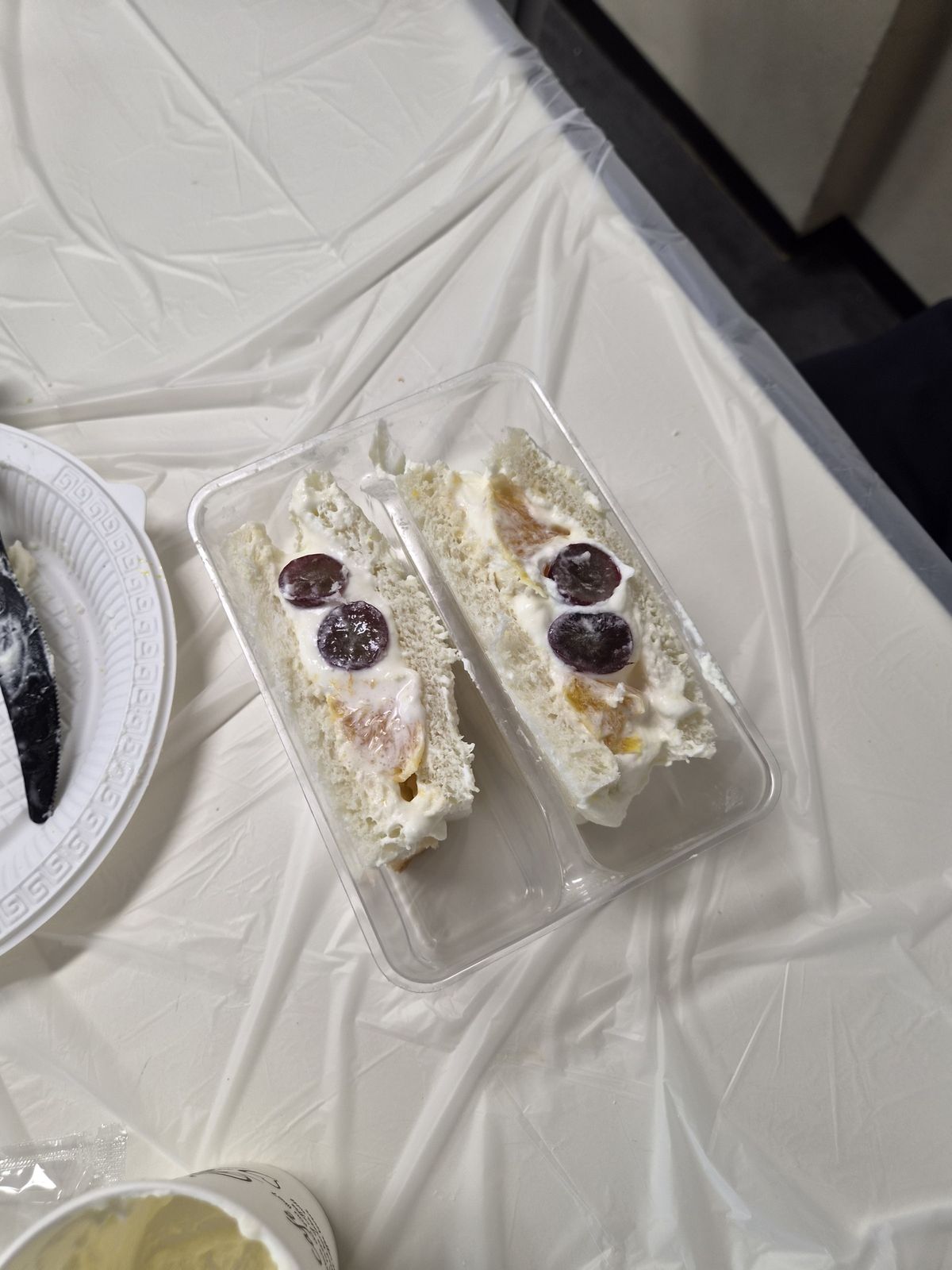 투명 용기 안 샌드위치 두 조각 — 흰 크림 사이로 과일 조각이 보이는 단면