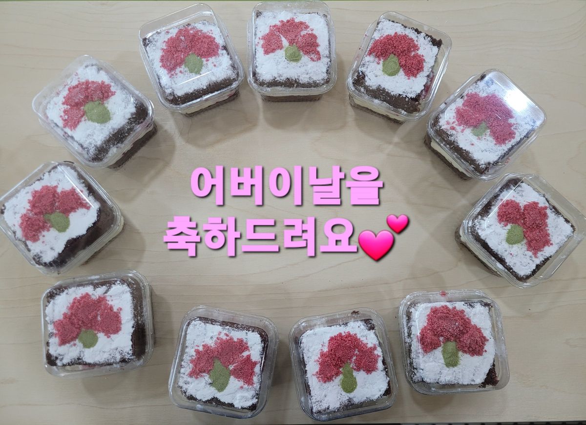나무 탁자 위 투명 용기에 담긴 케이크들이 둥글게 놓여 있고, 흰 가루 위에 분홍 꽃과 초록 잎 모양이 찍힌 모습