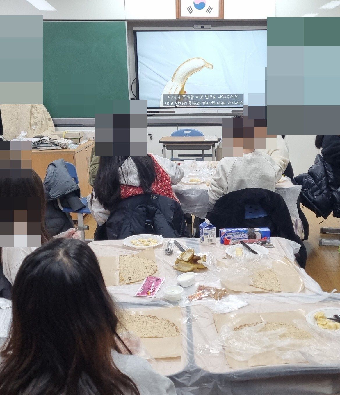 모둠 책상에 크레페와 바나나 접시를 올려 두고 앞쪽 전자칠판의 조리 영상을 보는 교실