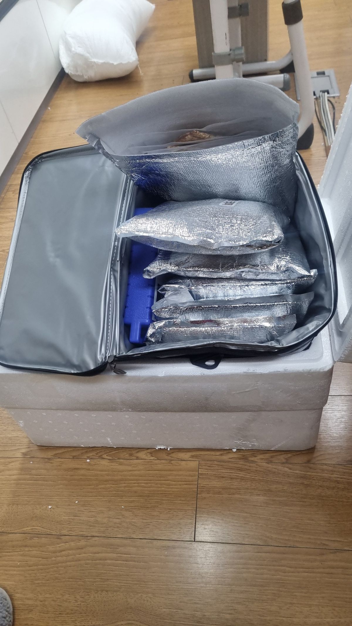 스티로폼 상자 위에 열린 보냉 가방, 그 안의 은색 보냉 파우치와 파란 아이스팩
