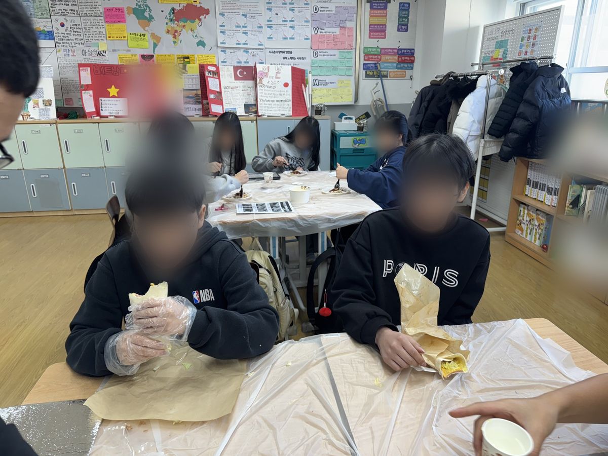 앞 모둠은 유산지에 싼 랩을 들고 있고 뒤 모둠은 접시를 앞에 두고 앉아 있는 교실 모습