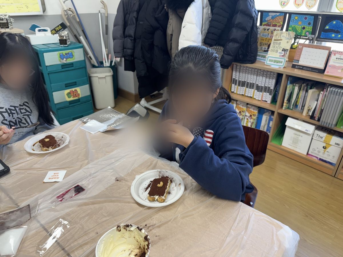 견과를 올린 티라미수 접시 앞에서 숟가락으로 한 입 뜨는 모습