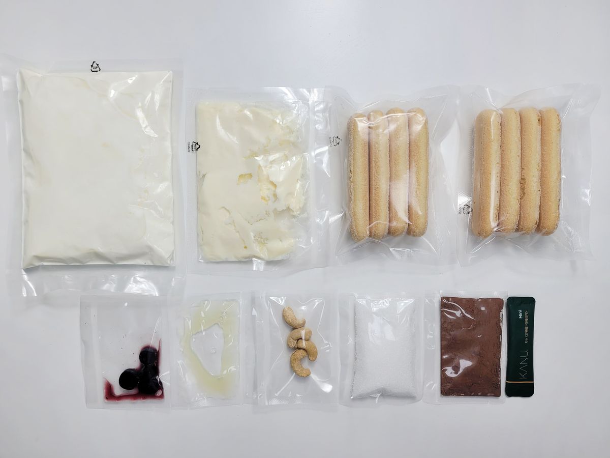 흰 바닥에 크림 봉지, 길쭉한 핑거쿠키, 작은 봉지 여러 개와 코코아 가루가 줄 맞춰 펼쳐져 있는 모습