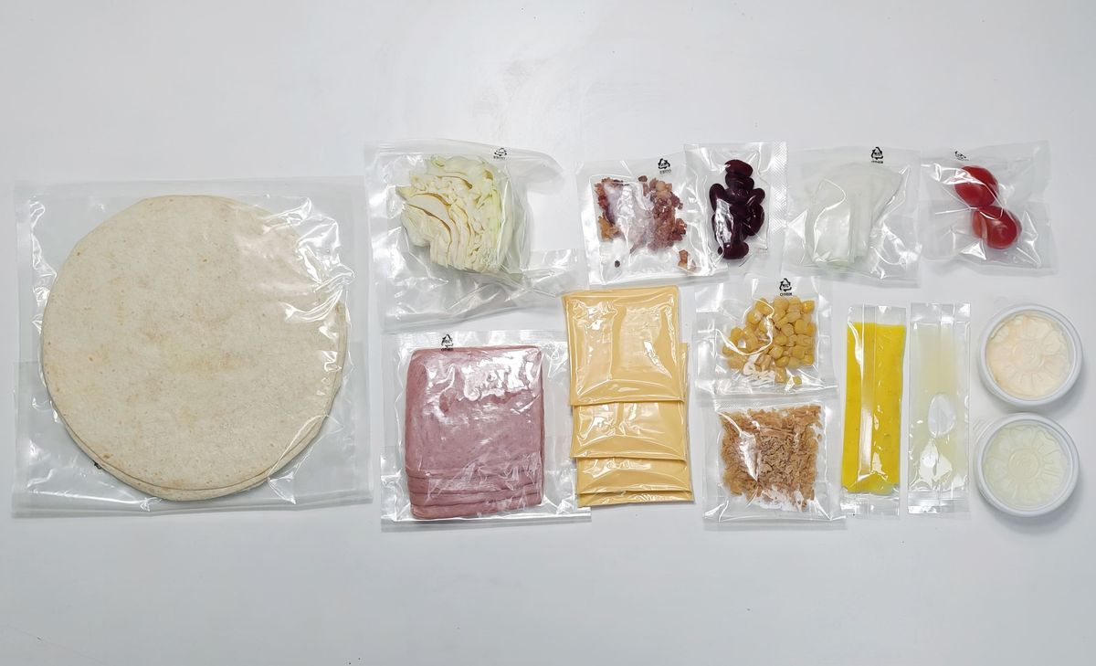 흰 바닥에 둥근 또띠아, 햄, 치즈, 작은 봉지와 소스 용기들이 줄 맞춰 펼쳐져 있는 모습