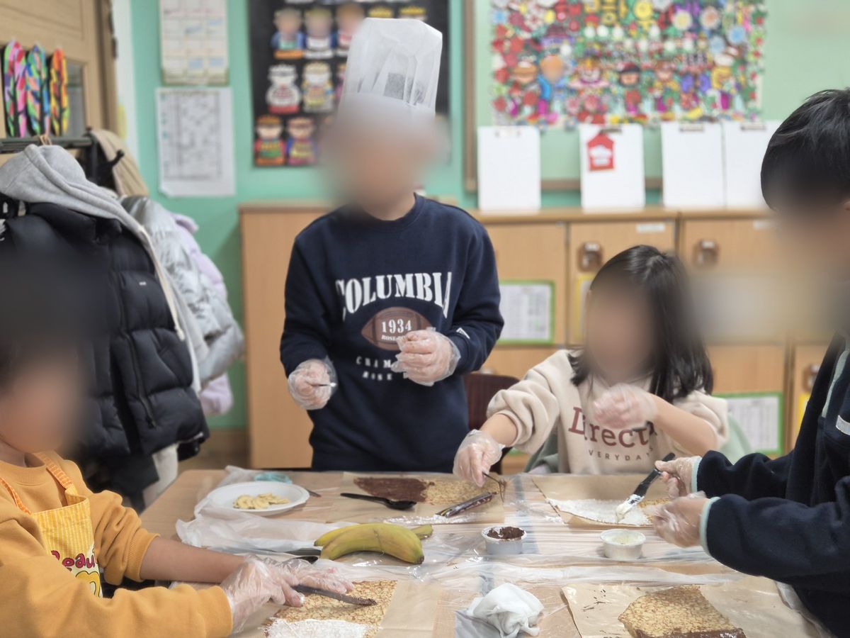 비닐장갑 낀 손들이 모둠 책상 위 크레페빵에 재료를 펴 바르는 모습