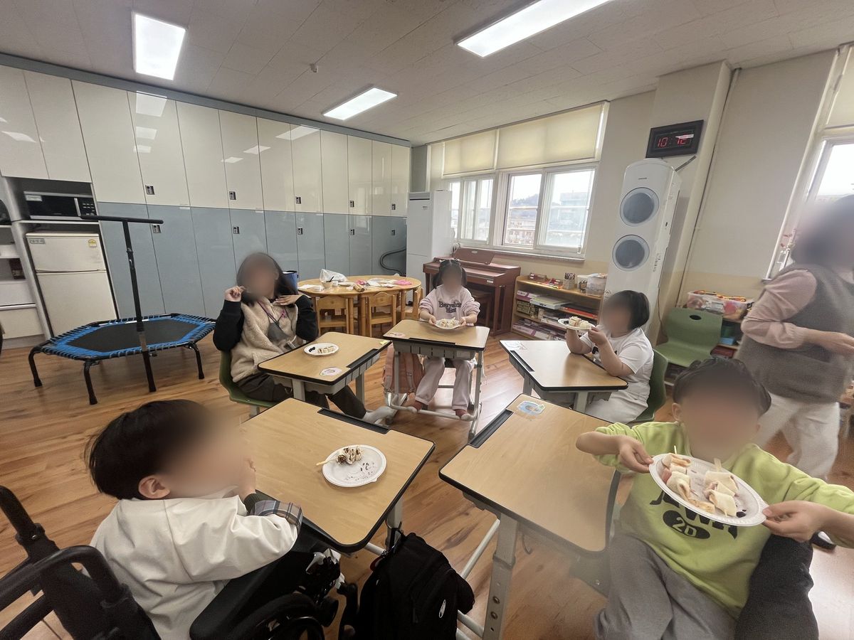 교실에서 아이들과 선생님들이 책상에 앉아 직접 만든 롤 꼬치를 들고 먹는 모습